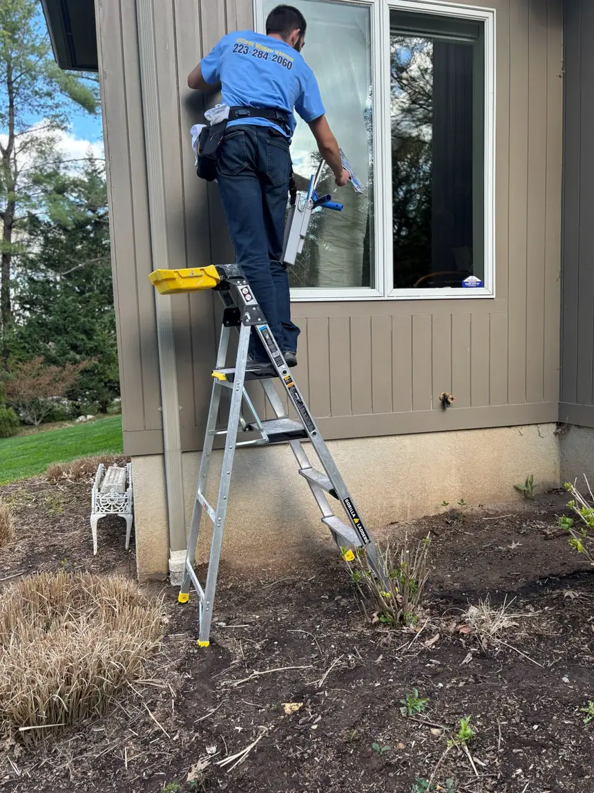 Wizards Window Washing technician in uniform cleaning a second-storey window from a ladder