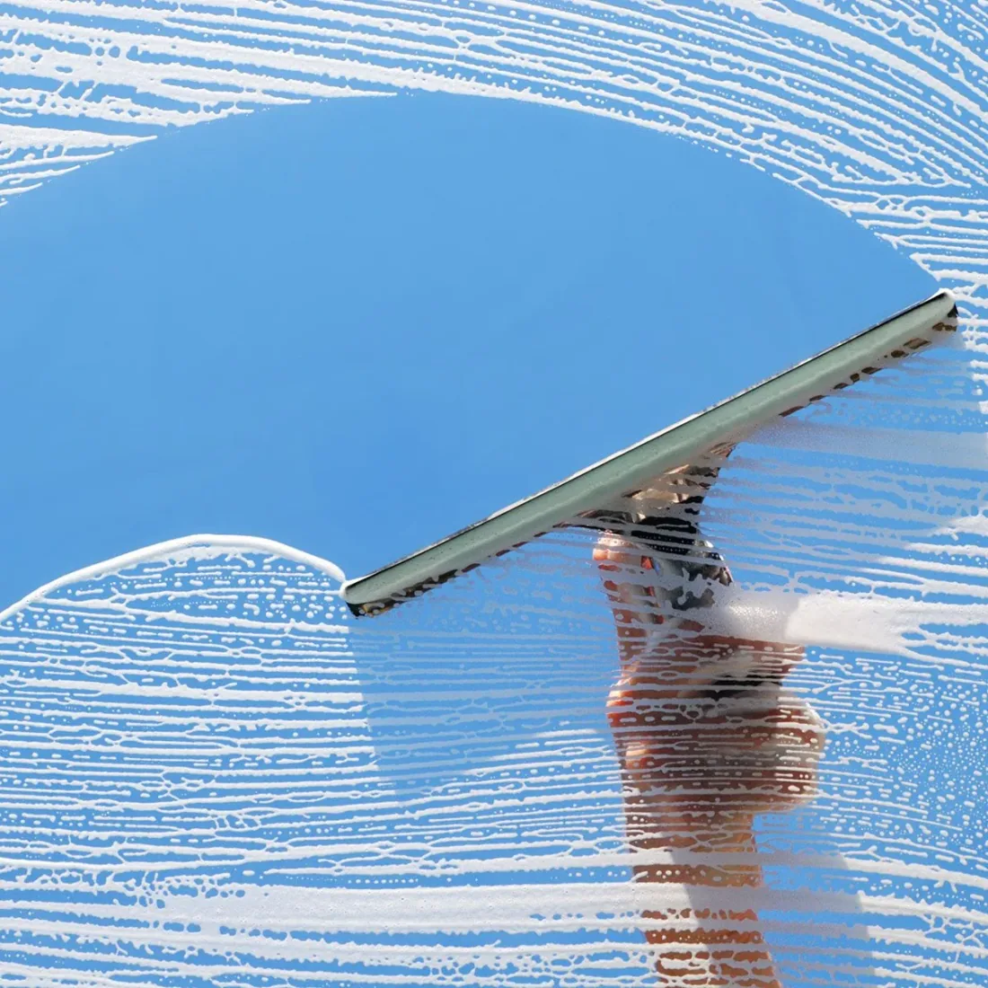 Squeegee pulling a clean stripe across soapy glass